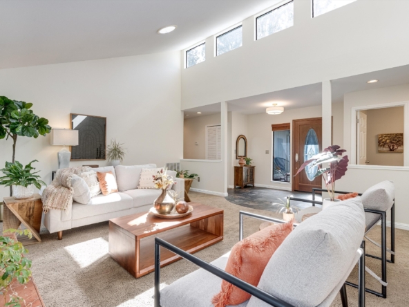 Bright living room with beige sofa, greenery, and a wooden coffee table bathed in natural light from tall upper windows.