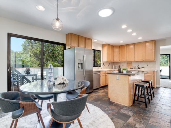 Bright kitchen with light wood cabinets, stainless steel refrigerator, and an island—sliding glass door to the patio on the left.