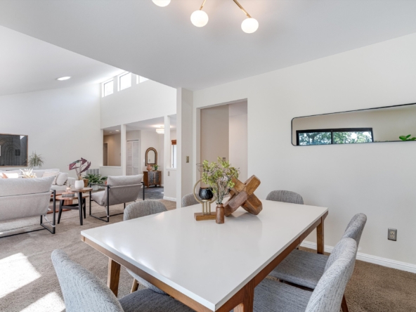 Bright open living and dining area with a white rectangular table and gray upholstered chairs.