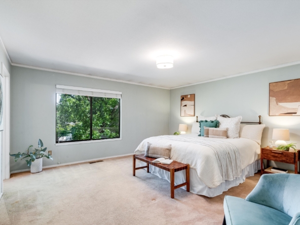 Bright bedroom with a large bed, matching nightstands, and a window showing green trees outside.