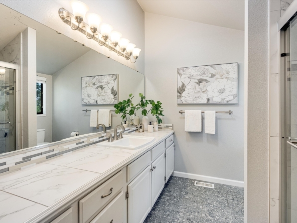 Modern bathroom with a double-sink vanity, marble countertops, and a row of globe light fixtures above the mirror.