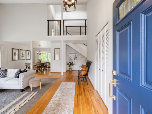 Open-concept living area with a blue front door on the right, white walls, and hardwood floors.