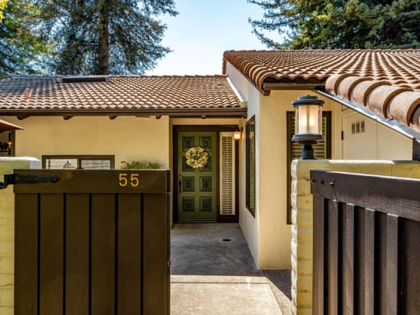 Front entrance of a beige house with a tiled, curved roof and dark wooden gates; the number 55 is visible on the gate.