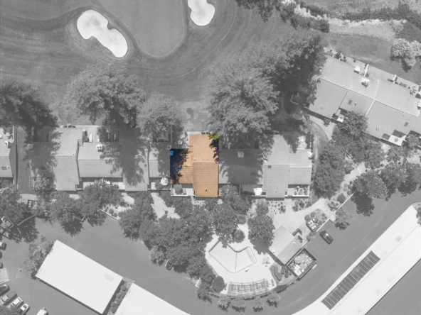 Aerial view of a golf course with sand bunkers and a nearby row of houses, including an orange-roofed building in the foreground.